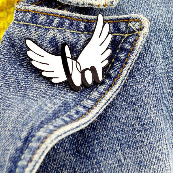 Little Angel enamel pin in the shape of wings with the LA logo